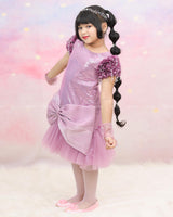 Shimmery Pink Dress With Satin Flower Sleeves Adorned With Pearl Tassels And A Large Bow Accent.