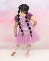 Shimmery Pink Dress With Satin Flower Sleeves Adorned With Pearl Tassels And A Large Bow Accent.