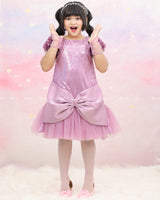 Shimmery Pink Dress With Satin Flower Sleeves Adorned With Pearl Tassels And A Large Bow Accent.